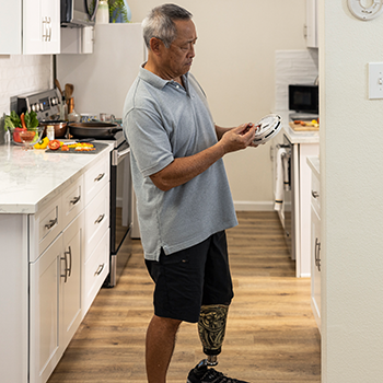 A man with a prosthetic leg changes the batteries in a kitchen smoke detector