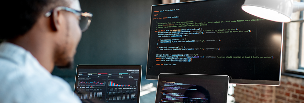 Male IT professional coding at home on multiple screens