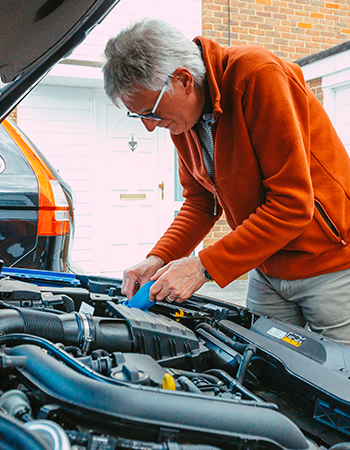 An older man checks his vehicle's oil and fluid levels under the hood