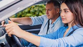 A teen girl focuses on her driving skills as she learns how to drive a car alongside an instructor in the passenger seat.