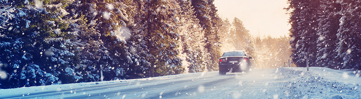 A black car driving on a snowy, icy road through a remote, wooded area.