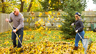 Two people in sweaters preparing their home for autumn by raking fallen leaves.