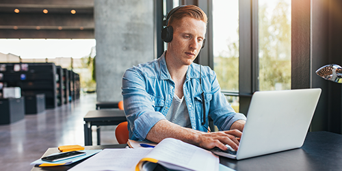 Young college student studying at a table with books and an open laptop.