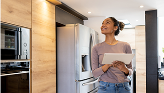 Woman using a tablet to control smart home appliances in the background, such as a refrigerator and a thermostat.