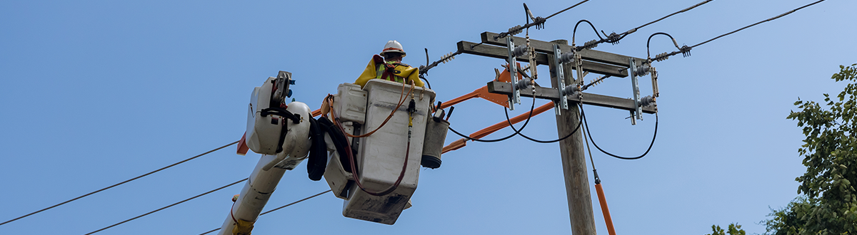 Electrical linemen working on a power pole from a cherry picker, repairing and moving electrical service lines.