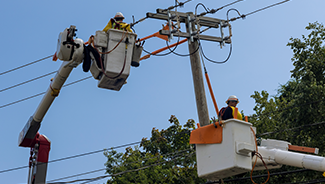 Electrical linemen working on a power pole from a cherry picker, repairing and moving electrical service lines.
