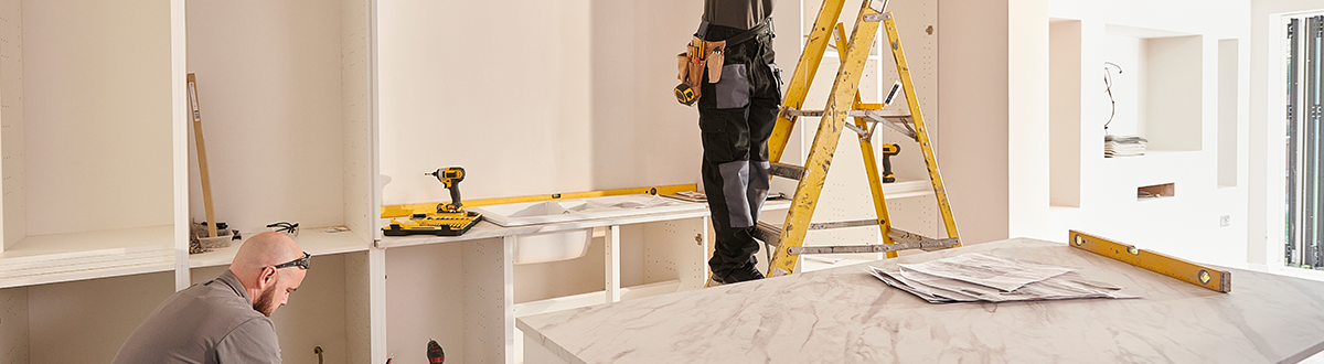 An electrician and a carpenter working on remodeling a kitchen with new cabinets and marble countertops.