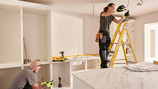 A female electrician and a male carpenter work on renovations during a home kitchen remodel.