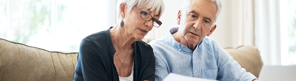 A senior couple going through their home insurance policy while sitting on the sofa at home.