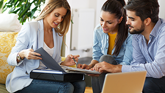 A man and a woman sitting on a couch with an agent, going over their insurance policies.
