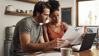 Cropped shot of a couple using their laptop and going through paperwork at home