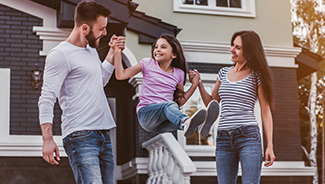 A man and a woman playfully lift and swing a young girl between them.